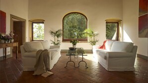 A spacious living room with two white sofas, a coffee table, and a large arched window providing a view of greenery.