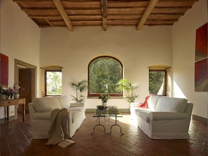 Relax in this spacious living room with two sofas, a glass coffee table, and a large window offering a view of lush greenery.