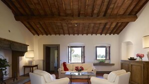 A spacious living room with a high wooden ceiling, two white sofas, a coffee table, and a view through large windows.