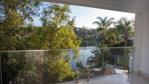 Ein Balkon mit Glasgeländer und Blick auf einen See, umgeben von Bäumen und einem Wohngebiet im Hintergrund.