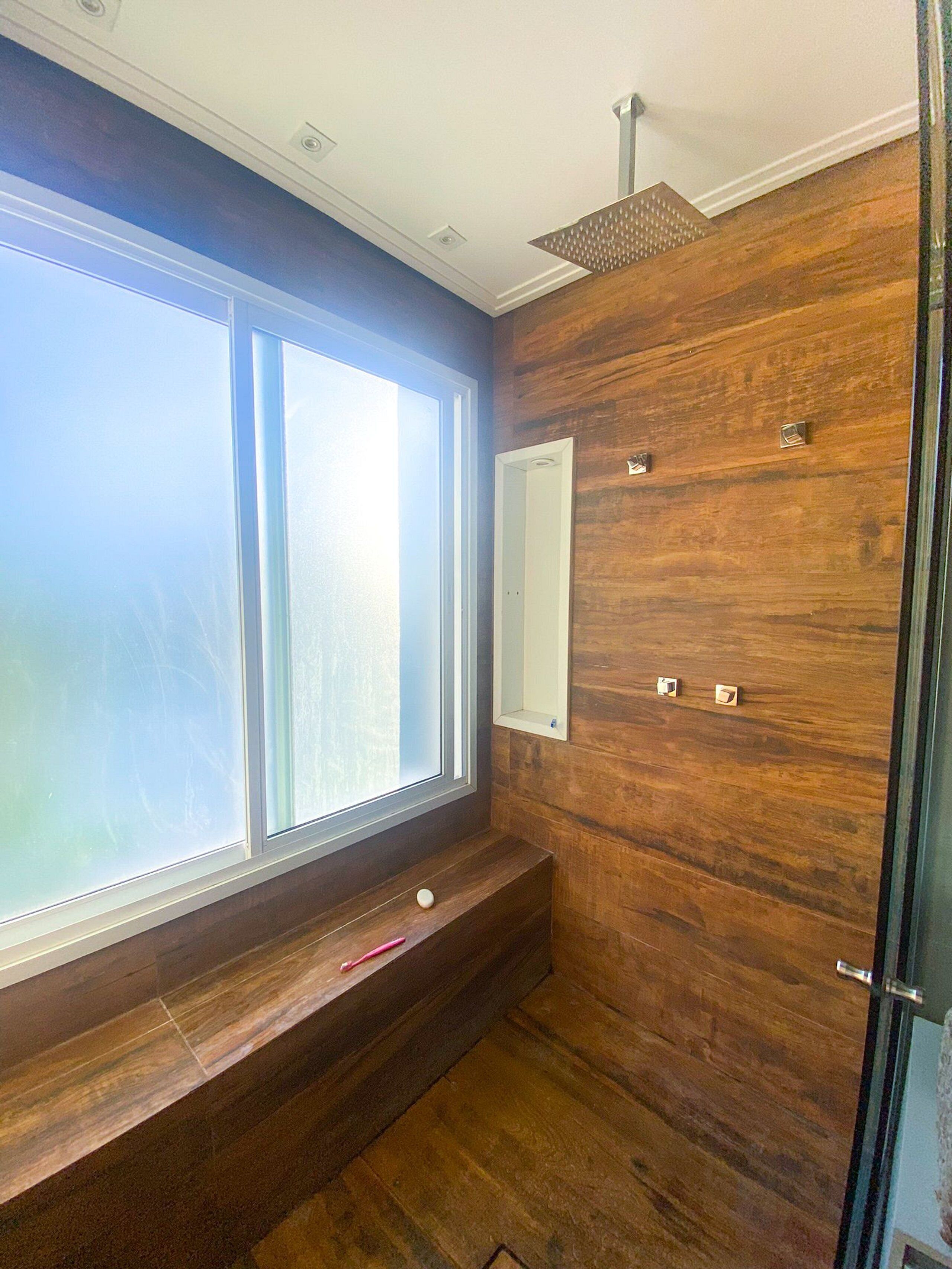 A modern bathroom with a large window, wooden paneling, a bench, and a shower area.