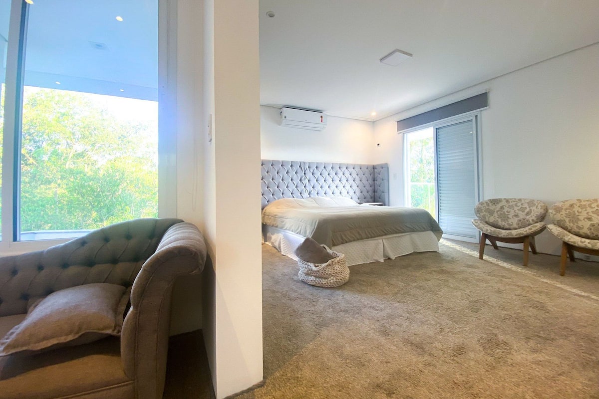 Un dormitorio moderno con una cama grande, un sofá, dos sillones y vistas a zonas verdes.