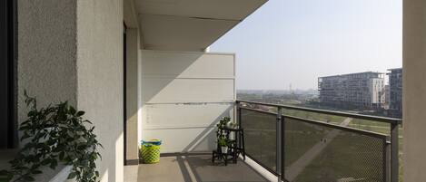 A balcony with a view of buildings, a potted plant, and a chair.