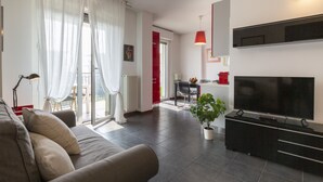 Un saló modern amb un sofà, una televisió de pantalla plana, una zona de menjador amb taula i cadires, i una planta en test.