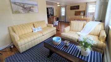 A living room with two yellow-striped sofas, a patterned rug, a wooden coffee table, and a painting of a beach scene.