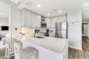A modern kitchen with white cabinetry, stainless steel appliances, and a central island with bar stools.