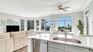 Una cocina moderna con lavavajillas, un comedor con mesa de vidrio y una sala de estar con sofá color beige.