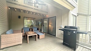 Un'area esterna coperta con mobili in vimini, un barbecue e una porta vetrata che dà su un balcone.