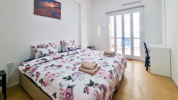 Un dormitorio con colcha estampada de flores, un cuadro en la pared y una puerta corrediza de vidrio que da a un espacio exterior.