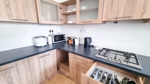 Una cocina compacta con armarios de madera, microondas, tostadora, hervidor y estufa a gas.