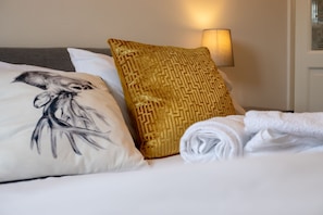 A neatly made bed with a patterned pillow, a white pillow with a bird design, and a rolled white towel. - 5star City Homes - Close to City Center, Free Wifi (Sunderland)