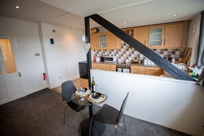 A modern kitchen with wooden cabinets, a microwave, and a dining area with a glass table and chairs. - 5star City Homes - Close to City Center, Free Wifi (Sunderland)