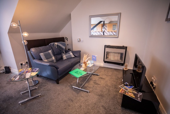 A modern living room with a grey sofa, a glass coffee table, a fireplace, and a television. - 5star City Homes - Close to City Center, Free Wifi (Sunderland)