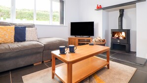A living room with a sofa, a coffee table, a television, and a fireplace. - Charlotte's House (Penzance)