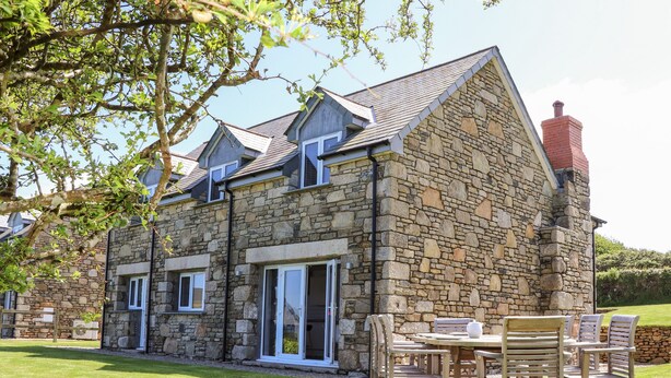 A stone house with a chimney, a lawn, and a patio with wooden furniture. - Charlotte's House (Penzance)