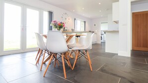 A modern kitchen with a dining area, large windows, and a clock on the wall. - Charlotte's House (Penzance)