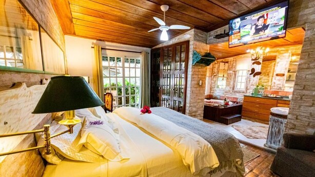 A cozy bedroom with a bed, a desk, a television, and a window. - Pousada Villa 3 Lagos (Santo Antonio do Pinhal)