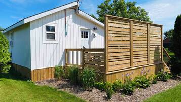 A single-story white building with a wooden deck and a fenced area with plants.
