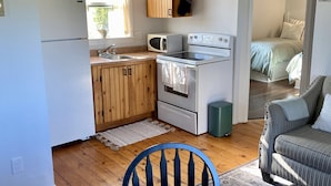 Une cuisine compacte avec des meubles en bois, un four à micro-ondes, un four traditionnel et un évier. On y trouve une table à manger avec une chaise et une plante en pot.