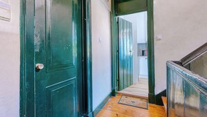 Un pasillo con puertas verdes, suelo de madera y felpudo.