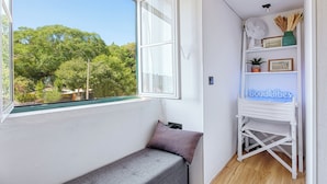 Una habitación pequeña con ventanal, un estante blanco con adornos y un banco.