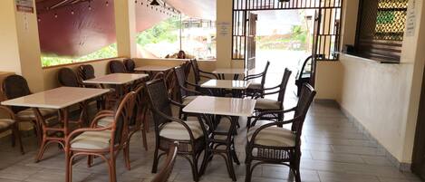 Un restaurante con mesas y sillas de madera, suelo de baldosas y vista al exterior a través de un ventanal.