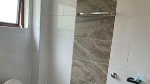 Un baño con inodoro, zona de ducha con pared de mármol y una ventana.