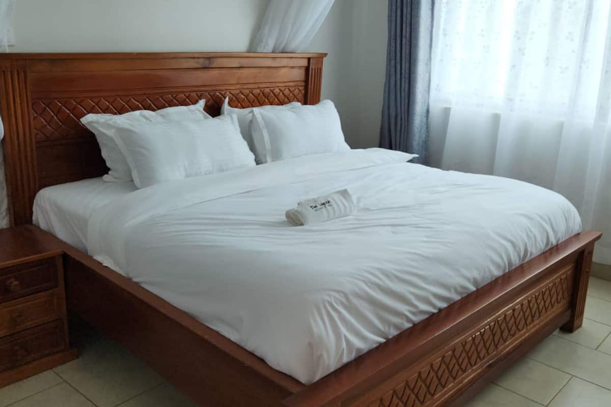A neatly made bed with white linens, a wooden headboard, and a wooden nightstand with drawers.