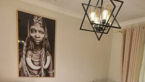 Una sala de estar con dos sillones, una mesa de centro blanca, un cuadro en la pared y una lámpara de techo geométrica.