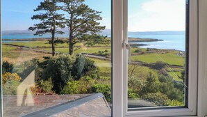 A window with a view of a coastal landscape, including a large tree and grassy fields. - Whispering Pines (Glanlough)