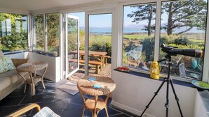 A room with a telescope, wicker furniture, and a view of the outdoors. - Whispering Pines (Glanlough)
