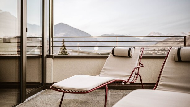 Ein Balkon mit zwei Loungestühlen, einer Glastür und Blick auf Berge.