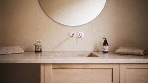 Ein Badezimmer mit einem runden Spiegel, zwei Handtuchhaken, einem Waschbecken und einer Flasche Duschgel.