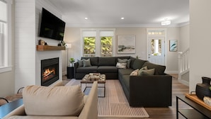 Ein modernes Wohnzimmer mit Kamin, großem Flachbildfernseher an der Wand, dunkelgrauem Ecksofa und Couchtisch.