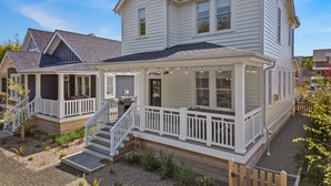 Ein zweistöckiges Haus mit überdachter Veranda, einer kleinen Terrasse und einem Grillbereich.