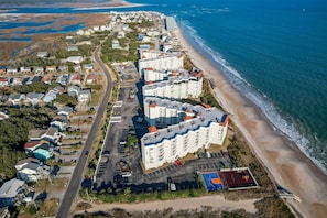 An aerial view of a coastal residential area with beachfront properties, a road, and a beach. - Dolphin's Den | Ocean Views + Community Pools (North Topsail Beach)