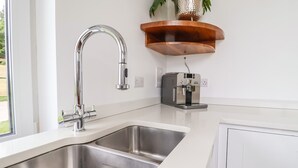 A modern kitchen with a stainless steel sink, a built-in coffee machine, and a wooden shelf above the counter. - Polly's Annexe (Ipswich)