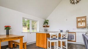 A modern kitchen with white cabinets, a wooden island, and two white chairs. - Polly's Annexe (Ipswich)