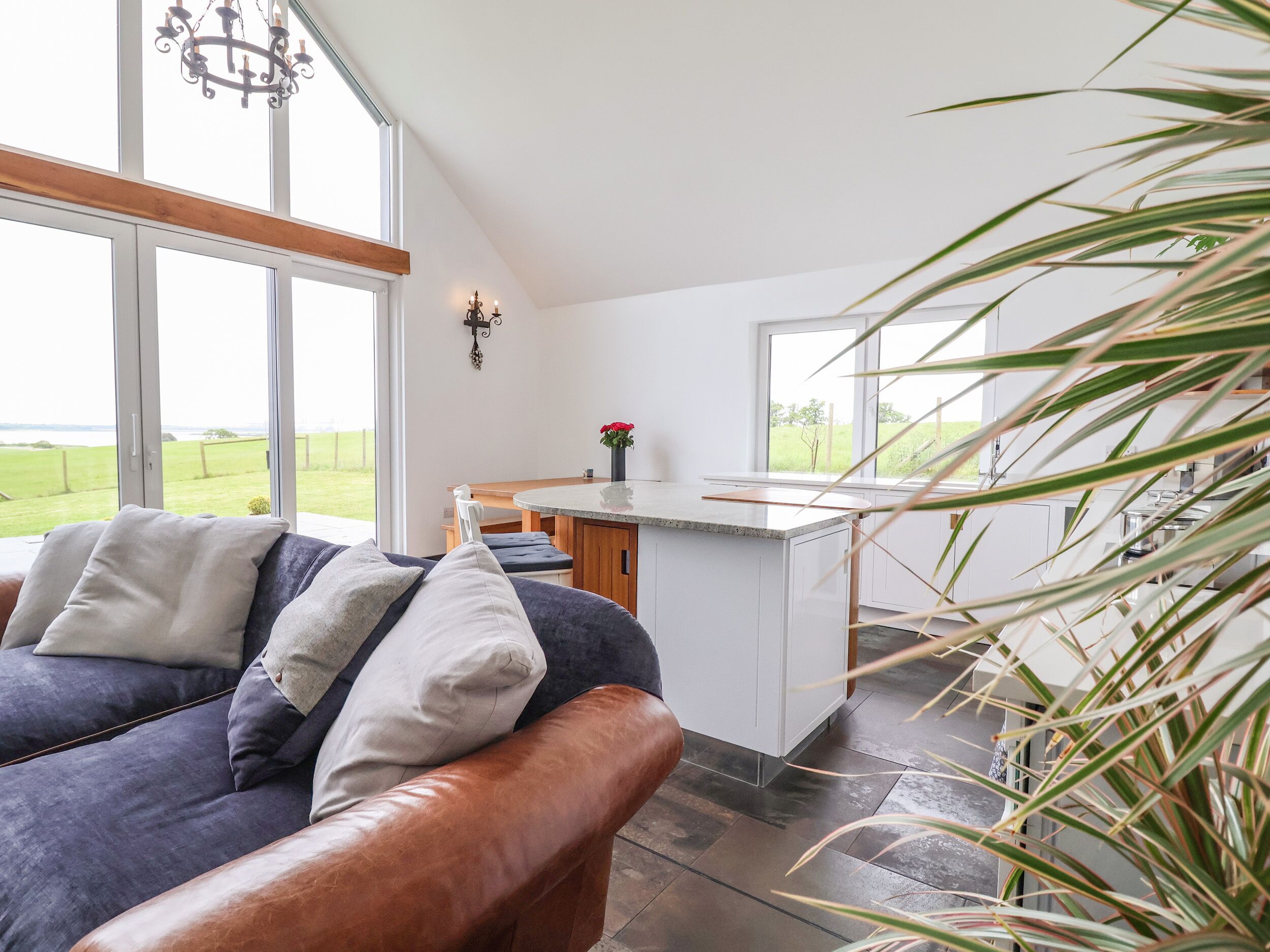 A modern living room with a large window, a sofa with cushions, and a kitchen area with a countertop and cabinets.