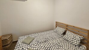 A small, single-bed room with a wooden headboard, a patterned bedspread, and a wall-mounted air conditioner. - Haus mit Garten 2 Minuten von Balaton (Siófok)