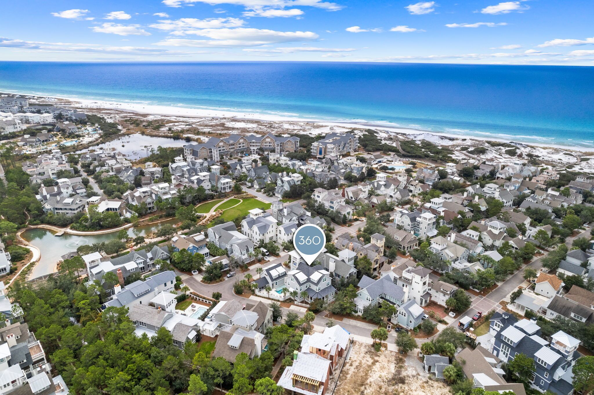 An aerial view of a coastal residential area with houses, a beach, and a lake.