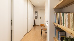 A hallway with a wooden floor, a chair, a bookshelf with books, and a door at the end. - notaMi - Dimora Certosa (Milan)