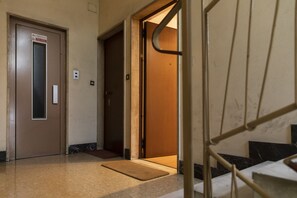 Un pasillo interior con una puerta de ascensor marrón, una puerta de madera y una barandilla de escalera metálica.