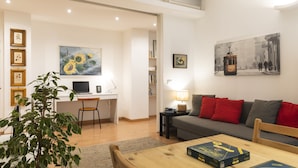 A modern living room with a desk, a sofa, and a dining table. There is a plant, a lamp, and artwork on the walls. - notaMi - Dimora Certosa (Milan)