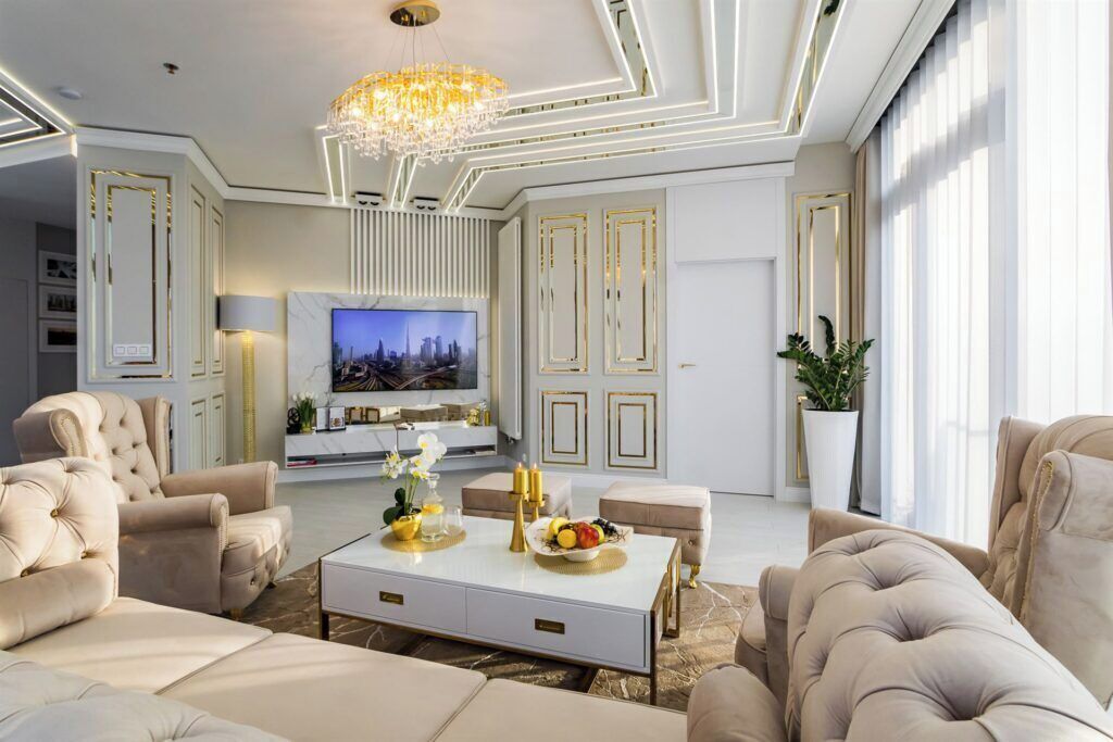 Ein luxuriöses Wohnzimmer mit großem Fernseher, bequemen Sofas, einem Couchtisch mit Obst und einer Kristallleuchtre.