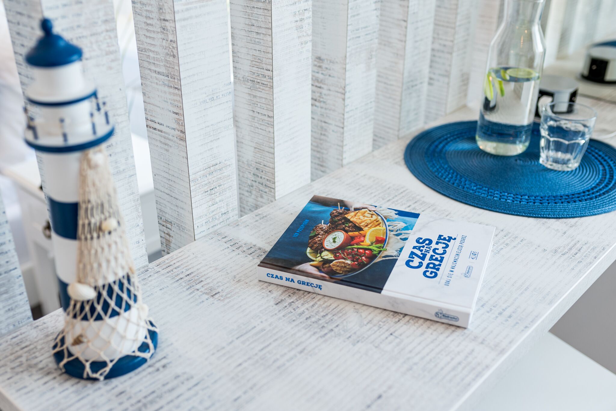 Um livro intitulado 'Czas na Grecji' sobre uma mesa com decoração náutica e uma garrafa de água.
