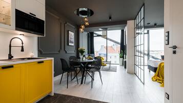 Een moderne keuken met gele kastjes, een zwarte afzuigkap, en een eethoek met een ronde tafel en zwarte stoelen.
