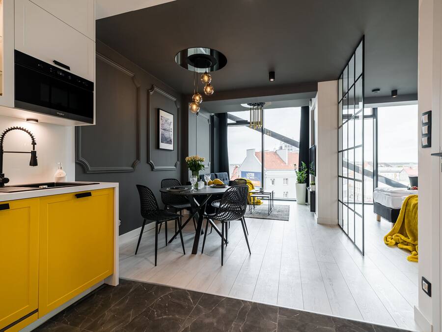 Een moderne keuken met gele kastjes, een zwarte afzuigkap, en een eethoek met een ronde tafel en zwarte stoelen.