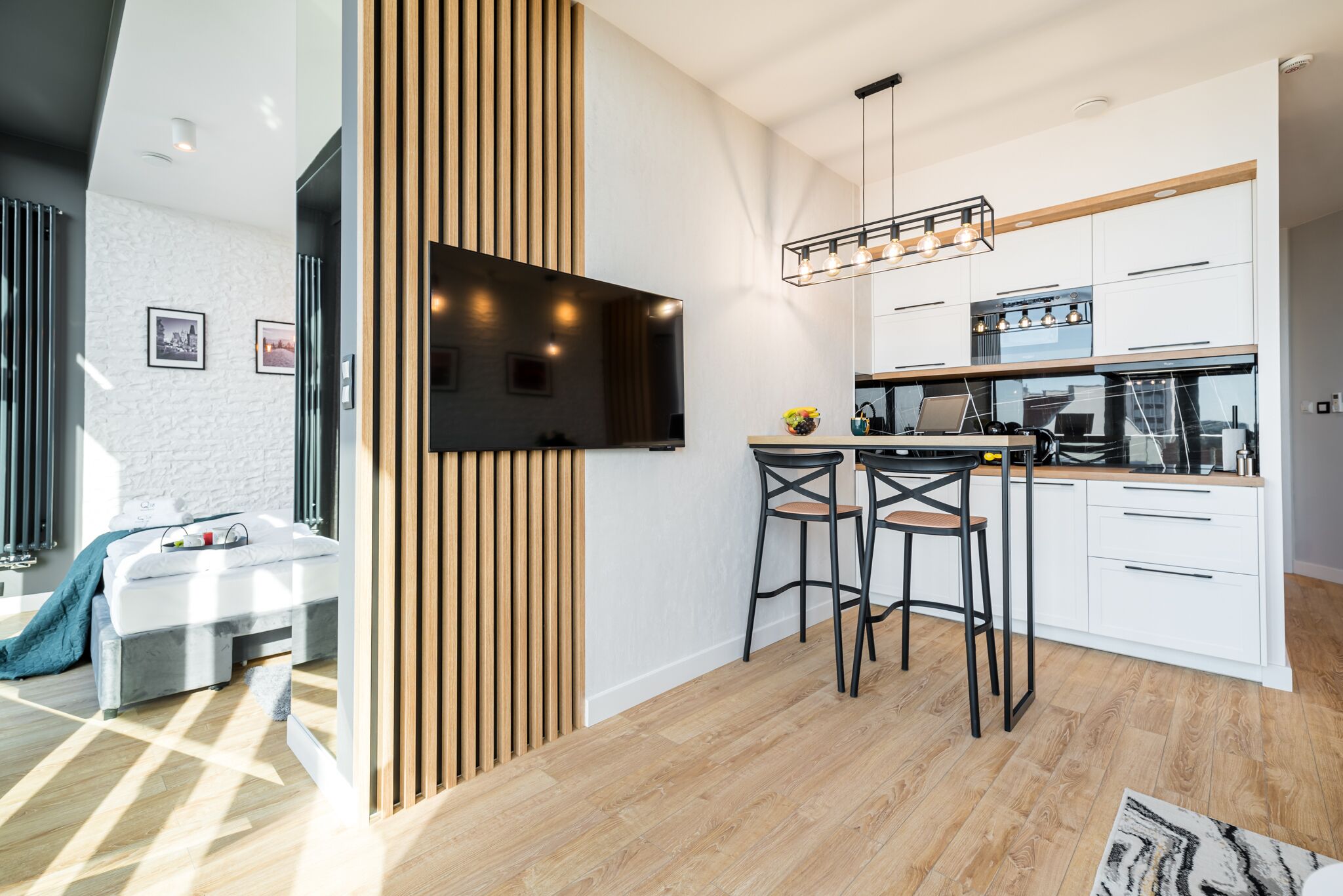 A modern kitchen with a built-in oven, a dining area with stools, and a large TV mounted on the wall.