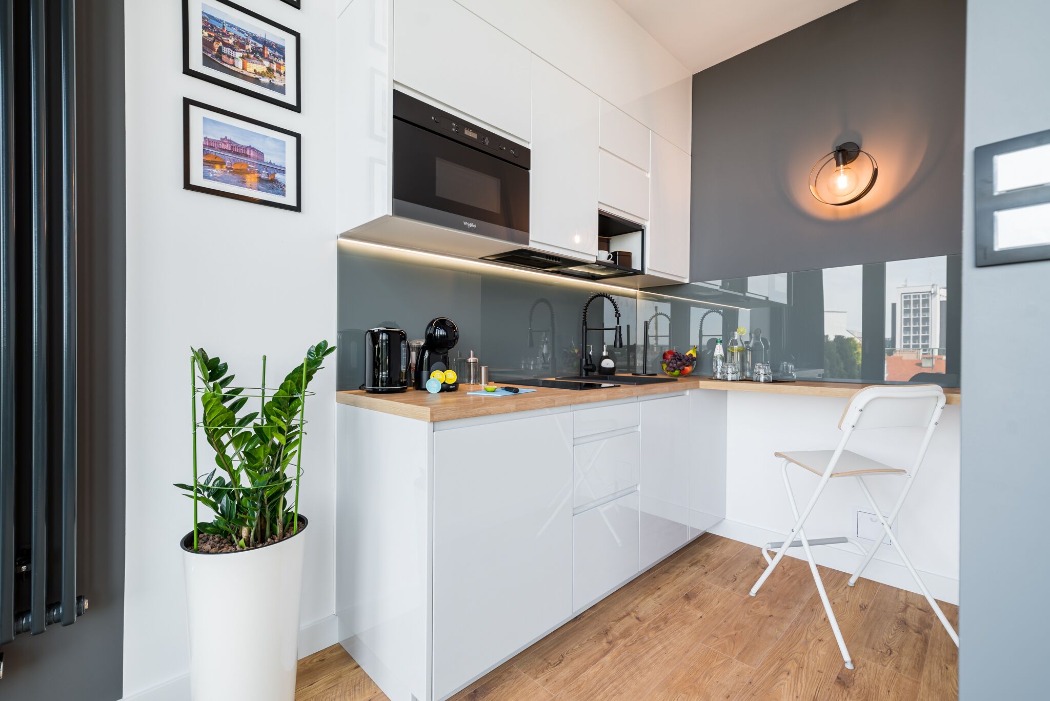 Una cocina moderna con armarios blancos, horno empotrado, cafetera y una planta en maceta.